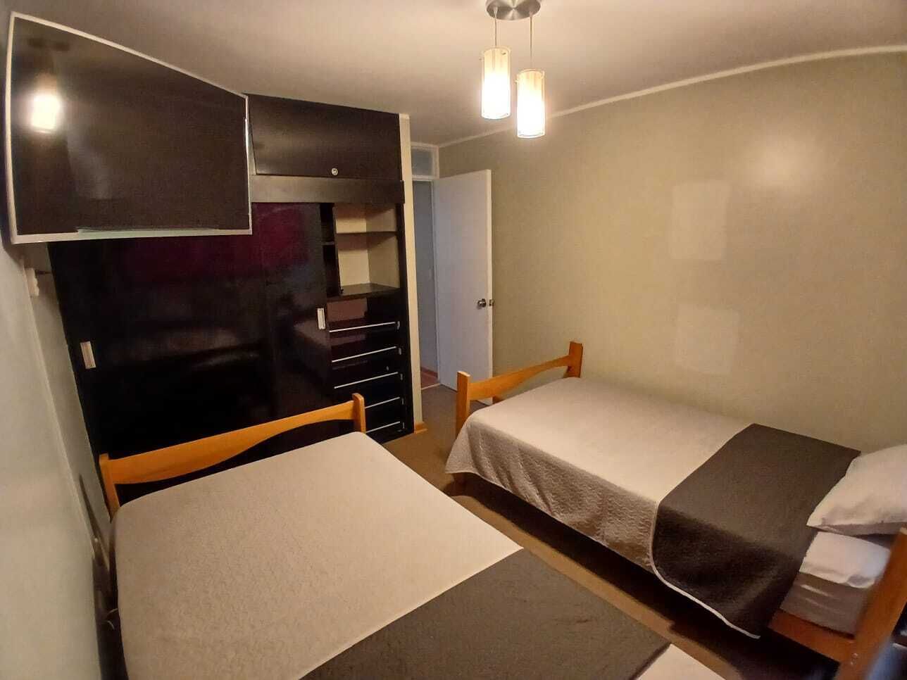 A bedroom with two single beds, a TV mounted on the wall, a wardrobe, and a door leading to another room.