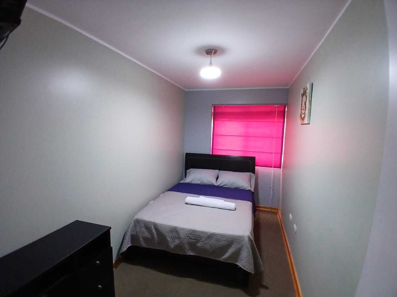 Et lille enkeltværelse med en seng, et natbord og et vindue med pink gardiner.