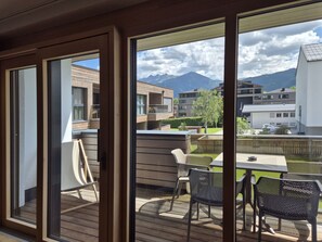 A balcony with a table and chairs, a view of buildings and mountains, and a wooden deck. - 3_SPA - Deluxe Panorama 521 by Interhome (Zell am See)
