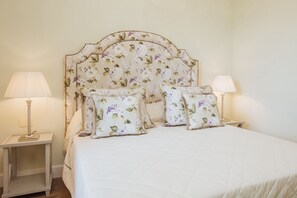 Een bed met een bloemrijk hoofdeinde, twee nachtkastjes met lampen, en een witte spreidek.