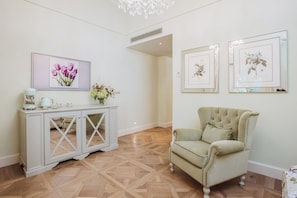A room with a white console table, a green armchair, and framed floral artwork on the wall. - Deluxe Junior Suite with Terrace & Balcony in Sorrento Center (Sorrento)