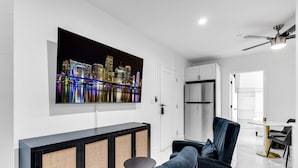 Un salón moderno con un televisor de pantalla plana grande, un sofá, una mesita redonda y un mueble con frente de fibras trenzadas.