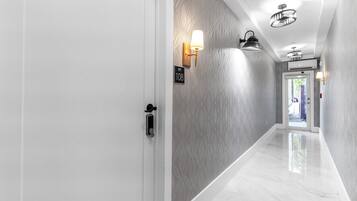 Un couloir avec une porte blanche, une plaque indiquant le numéro « 108 », et des luminaires fixés au mur.