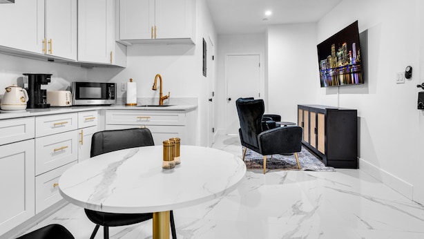 Una cocina moderna con armarios blancos, encimera de mármol y un comedor con mesa y sillas redondas.