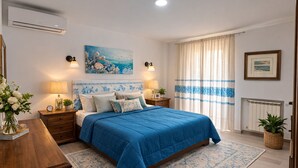Quarto com cama, mesas de cabeceira, um quadro, janela com cortinas e radiador.