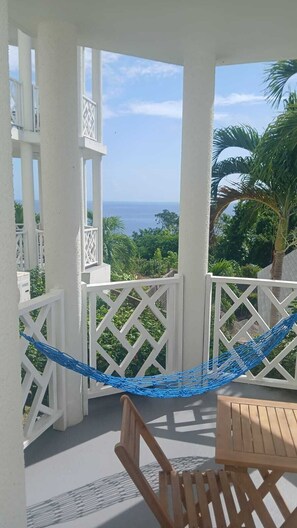 Un balcone con un'amaca, mobili in legno e vista sull'oceano.