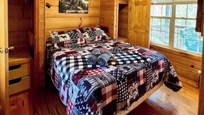 Un dormitorio de cabaña de madera con una cama, un ventilador de techo, una ventana y una puerta.
