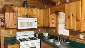 Una cocina compacta con armarios de madera, un microondas, una estufa y un lavamanos.