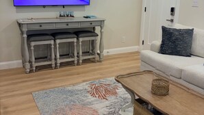 Una sala de estar con televisor de pantalla plana, un sofá blanco, una mesa de centro y un tapete estampado.