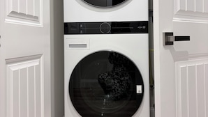 Una lavadora y secadora apiladas en un pasillo con puertas blancas.