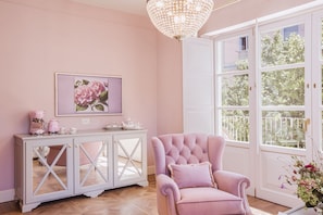 A room with a pink theme, featuring a tufted armchair, a white cabinet with glass doors, and a large window with a view of greenery. - Executive Suite with Terrace in Sorrento Center (Sorrento)