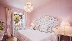 A bedroom with a large bed, a chandelier, a nightstand, and a window with curtains. - Executive Suite with Terrace in Sorrento Center (Sorrento)