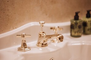 Ein Waschtisch mit zwei goldenen Wasserhähnen und zwei grünen Flaschen im Hintergrund.