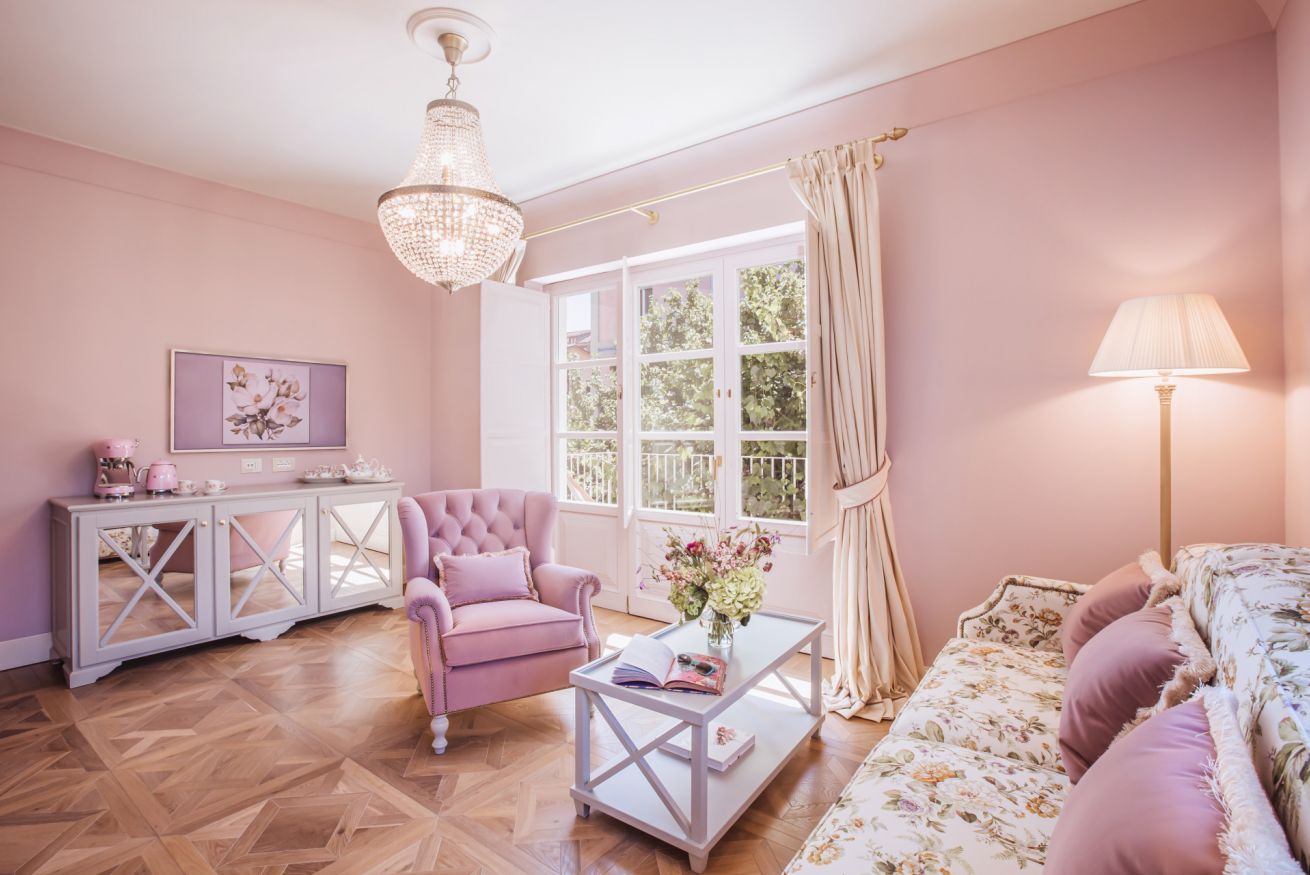 En stue i pink med lysekrone, sofa, lænestol, sofabord og skab.