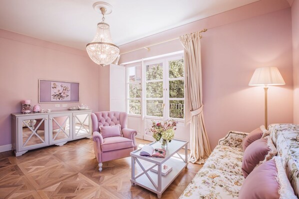 Ein salon in Rosa mit einer Deckenleuchte, einem Sofa, einem Sessel, einem Couchtisch und einem Schrank.