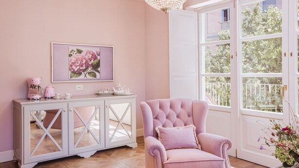 A room with a pink theme, featuring a tufted armchair, a white cabinet with glass doors, and a large window with a view of greenery. - Executive Suite with Terrace in Sorrento Center (Sorrento)