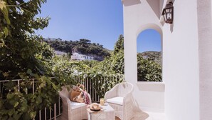 A balcony with wicker furniture, a white wall, and a view of a hillside. - Executive Suite with Terrace in Sorrento Center (Sorrento)
