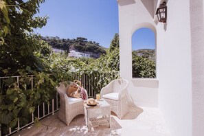Ein Balkon mit Korbmöbeln, einer weißen Wand und Blick auf eine Hügelkette.