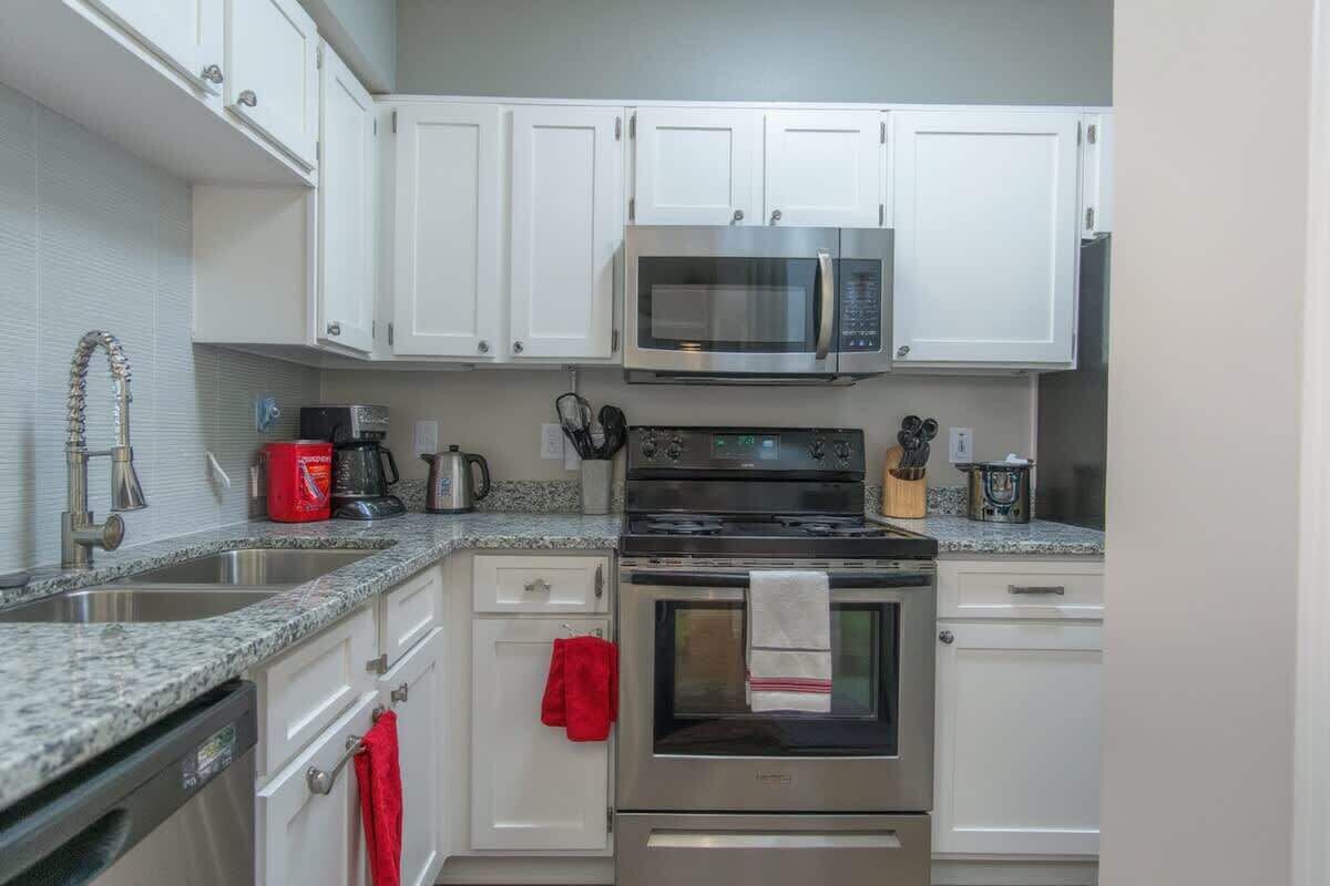 A kitchen with white cabinets, a stainless steel microwave, an oven, and a granite countertop.