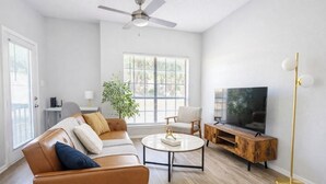 A living room with a sofa, coffee table, TV stand, and a ceiling fan. - Boulevard Stays Quiet 1BR King Suite, Pool Access, Gym (Irving)