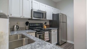 A modern kitchen with white cabinets, stainless steel appliances, granite countertops, and a double sink. - Boulevard Stays Quiet 1BR King Suite, Pool Access, Gym (Irving)