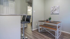 A modern kitchen with a bar stool, a wooden bench, and a small table with a plant. - Boulevard Stays Quiet 1BR King Suite, Pool Access, Gym (Irving)