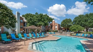 A swimming pool with blue lounge chairs and a brick building in the background. - Boulevard Stays Quiet 1BR King Suite, Pool Access, Gym (Irving)