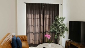 A living room with a sofa, a coffee table, a TV, and a plant. - Boulevard Stays Quiet 1BR King Suite, Pool Access, Gym (Irving)