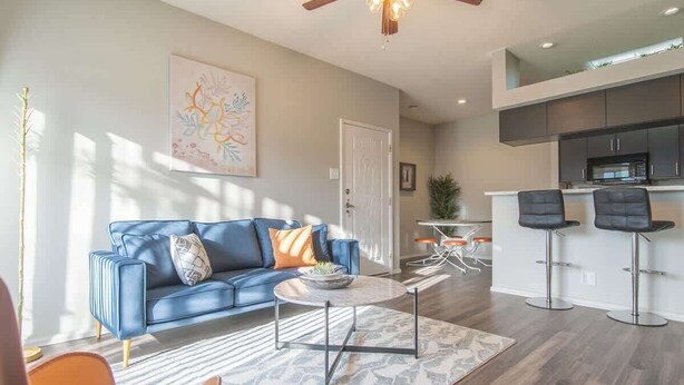A modern living room with a blue sofa, a coffee table, and a kitchen area with bar stools. - Boulevard Stays Quiet 1BR King Suite, Pool Access, Gym (Irving)
