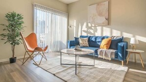 A living room with a blue sofa, a wooden rocking chair, a coffee table, and a potted plant. - Boulevard Stays Quiet 1BR King Suite, Pool Access, Gym (Irving)