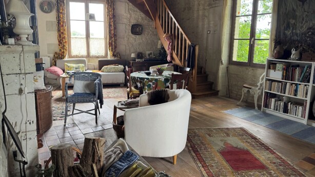 Une pièce rustique avec un escalier en bois, un fauteuil blanc, une table à manger et une bibliothèque.