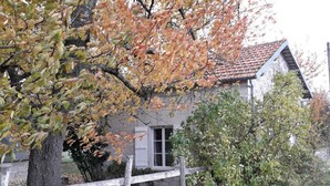 Un bâtiment rustique avec une façade en pierre, une clôture en bois et un arbre aux feuilles d’automne.