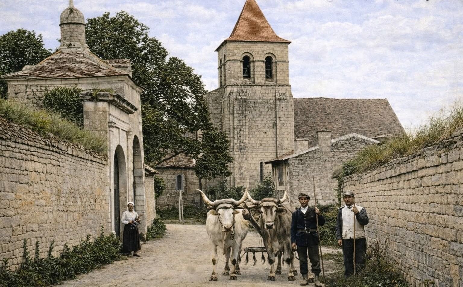 A stone building with a tower, a pathway, and two oxen with people standing beside them.