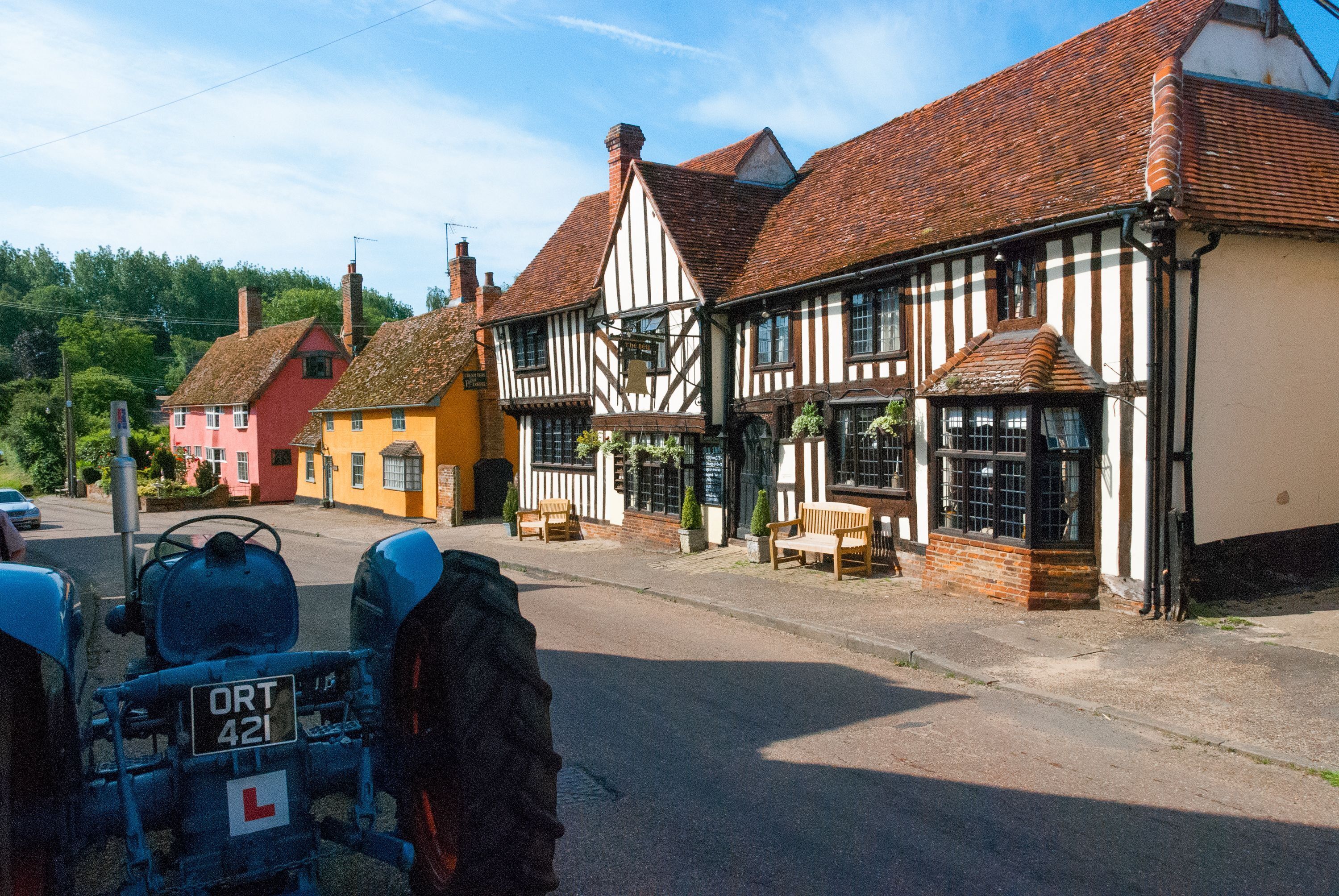 A traditional half-timbered building with a signboard, a bench, and a parked vehicle.