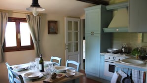 Un coin repas avec une table dressée pour quatre personnes, une cuisine avec des meubles de couleur bleu clair et une fenêtre avec des rideaux.