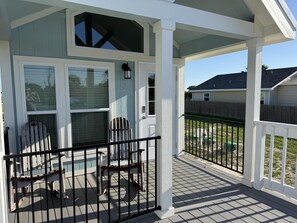 En overdækket veranda med to Adirondack-stole, et lille bord og et vindue med udsigt til et hus i nærheden.