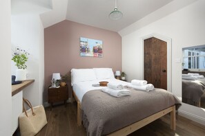 Ein Schlafzimmer mit Bett, Nachttisch, Wandlampe, Gemälde, Holztür und Fenster.