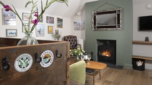 A cozy living room with a fireplace, wooden furniture, and wall-mounted artwork. - St Clements Cottage - Free WiFi - Outdoor kitchen and shower - Wood Burner (Mousehole)