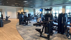 Ein geräumiges Fitnessstudio mit verschiedenen Trainingsgeräten, großen Fenstern und einem modernen Deckenstil.