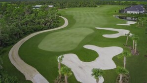 Ein Golfplatz mit Sandbunkern, einer gepflegten Spielbahn und einem Clubhaus im Hintergrund.