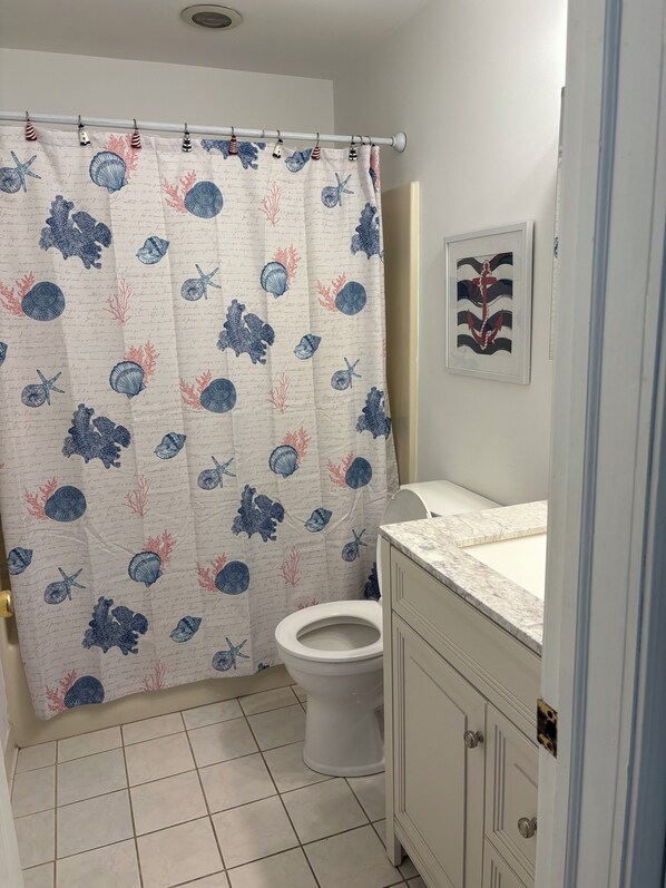 A bathroom with a shower curtain featuring a nautical theme, a toilet, and a marble countertop. - Cozy 2-bedroom condo right on the Wildwood boardwalk. (Wildwood)