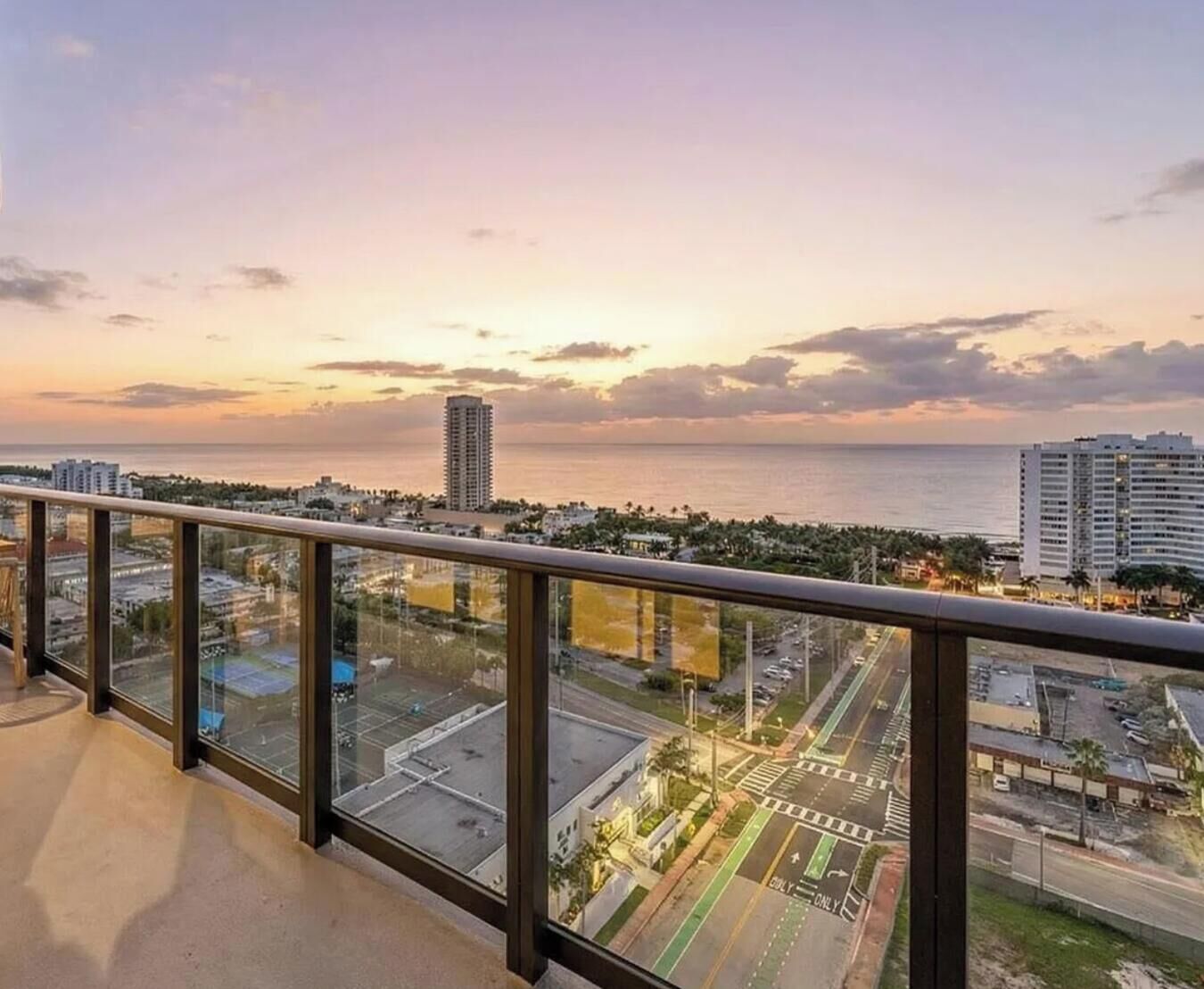 A balcony with a view of a cityscape and the ocean at sunset.