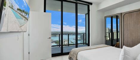 Un dormitorio con una cama grande, un ventanal corredero a un balcón con vista al mar y un cuadro en la pared.