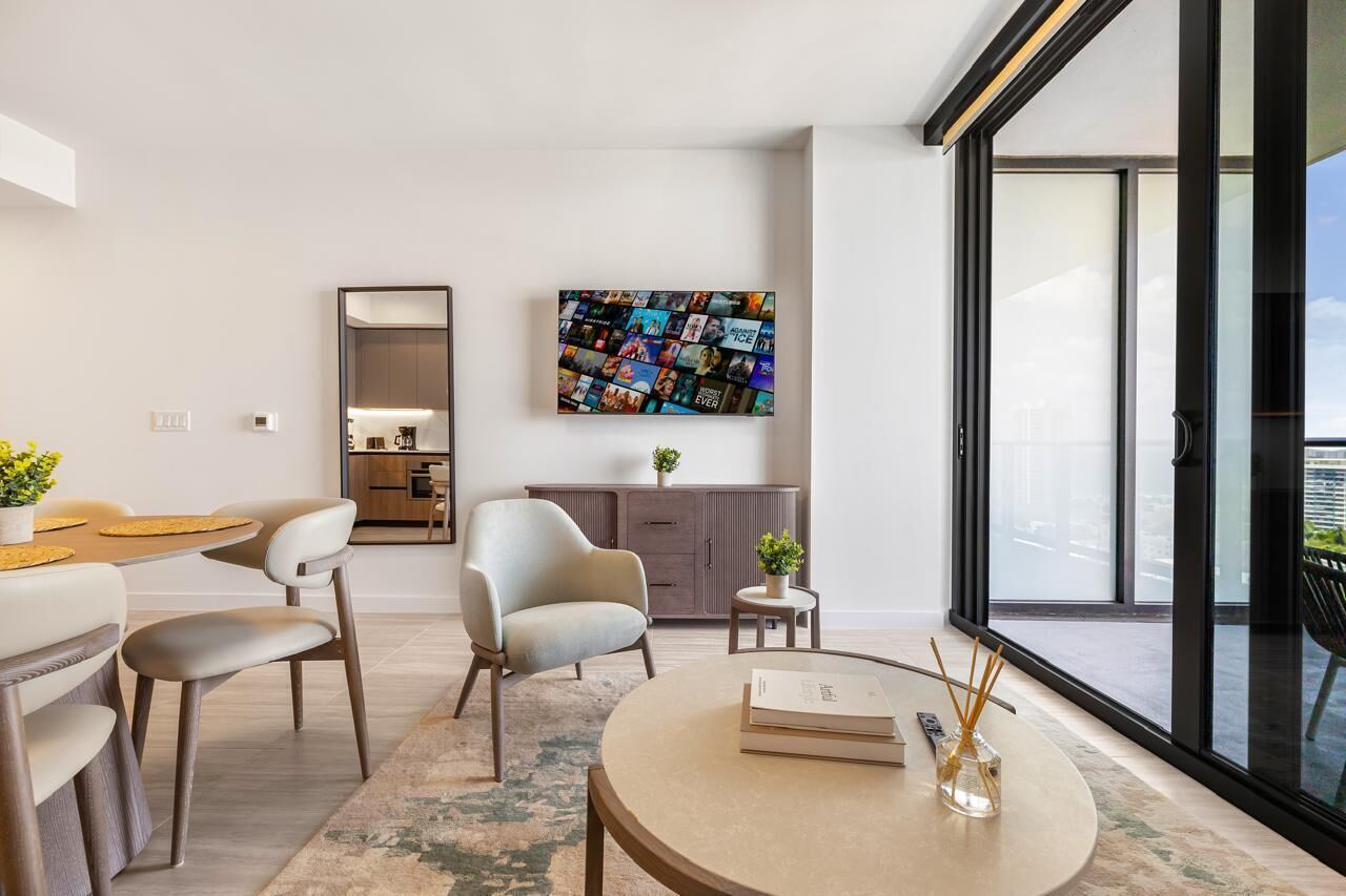A modern living room with a sofa, chairs, a coffee table, a TV mounted on the wall, and a balcony with a view.