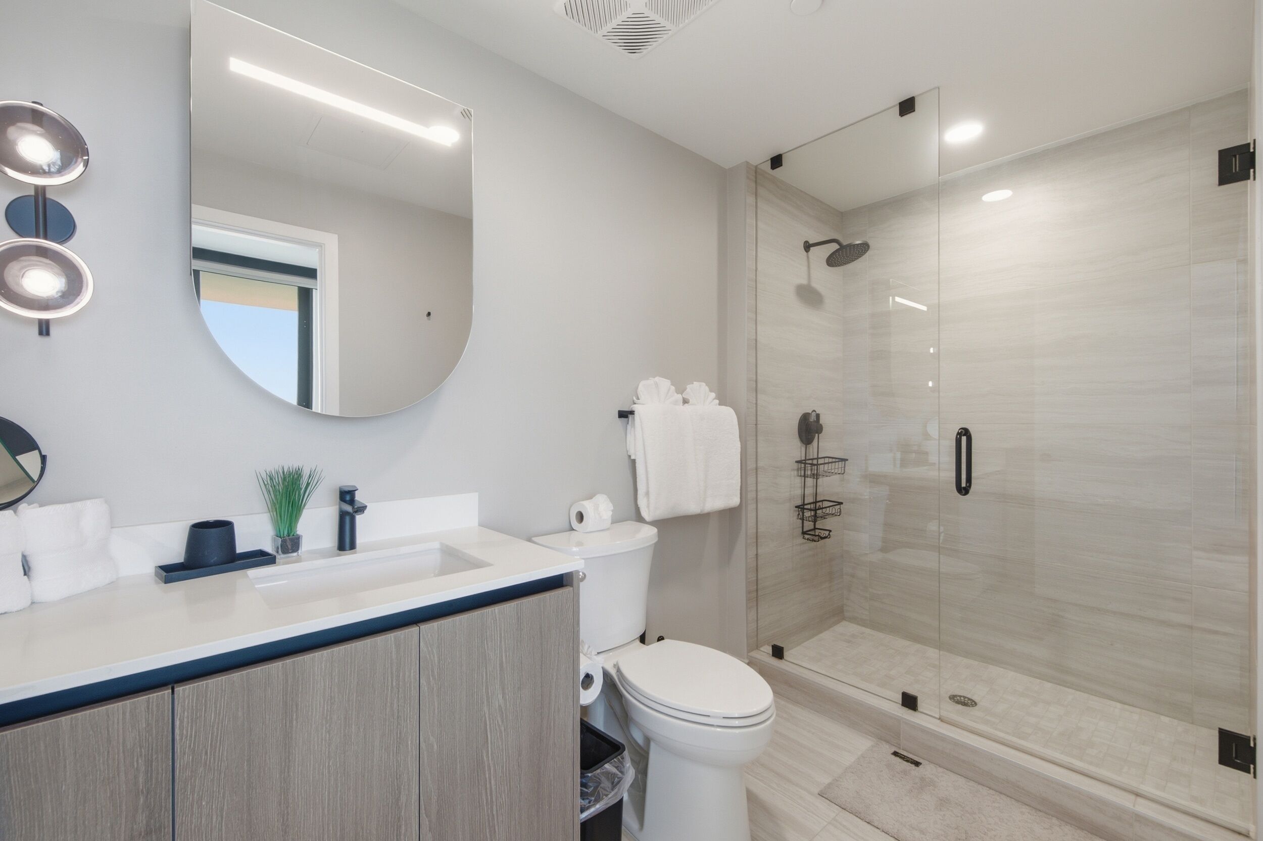 Un baño moderno con ducha de vidrio, lavamanos con espejo y retrete.