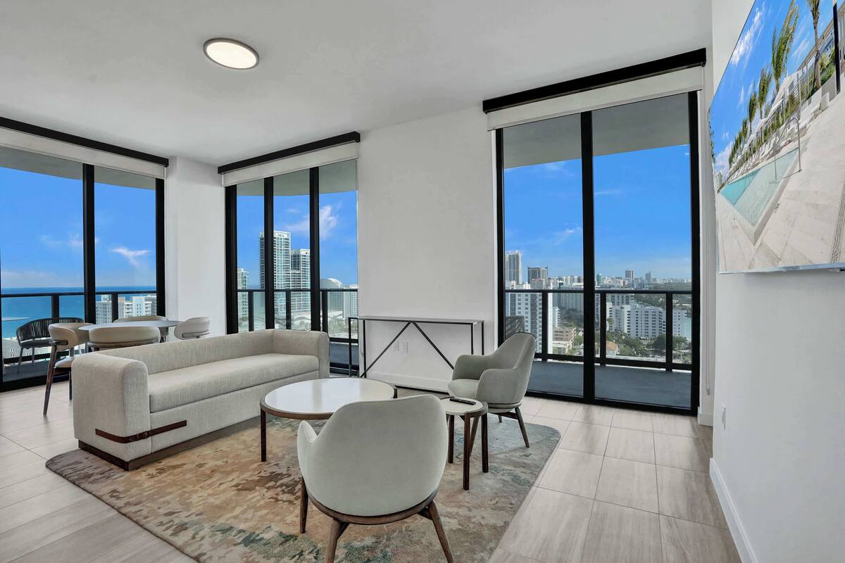 Una sala de estar moderna con sofá, sillas, una mesa de centro y grandes ventanales con vista a la ciudad.