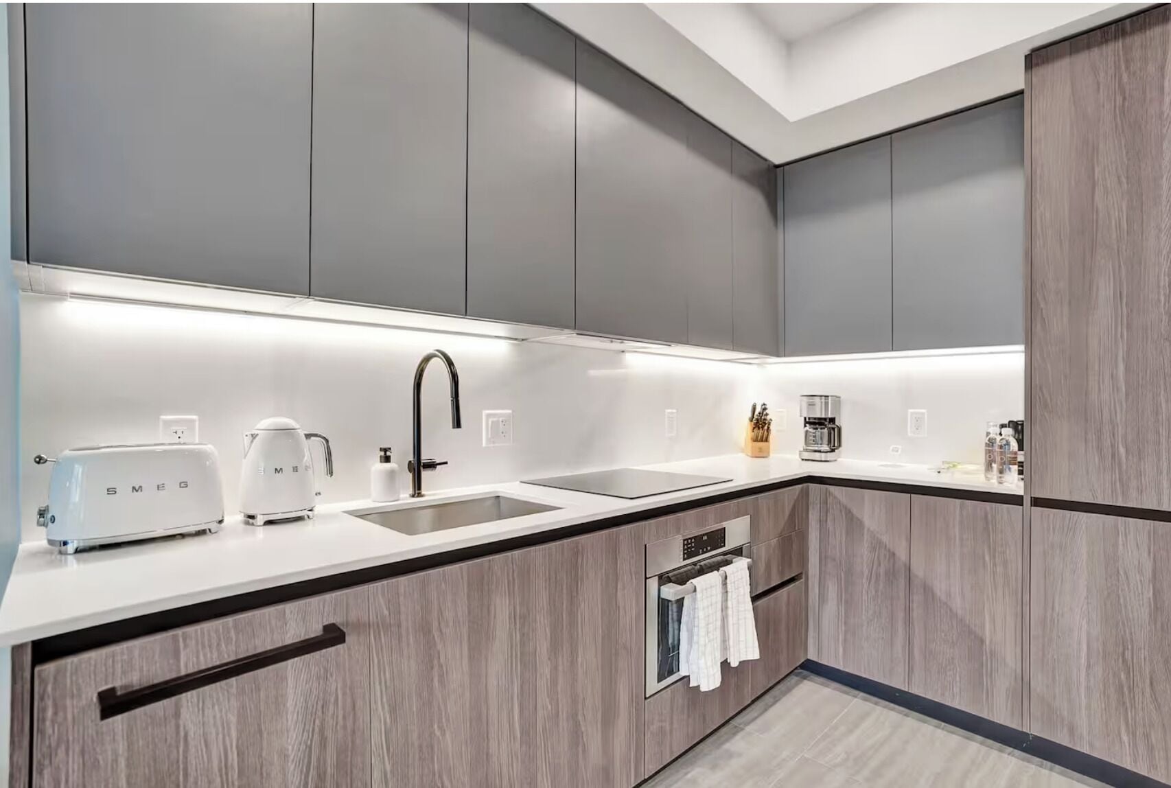 A modern kitchen with grey cabinets, a white countertop, a built-in oven, a coffee machine, and a toaster.