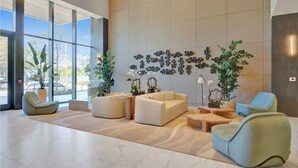 Eine großzügige Lobby mit großen Fenstern, einer Sitzecke mit Sofas und Sesseln sowie dekorativer Wandgestaltung.