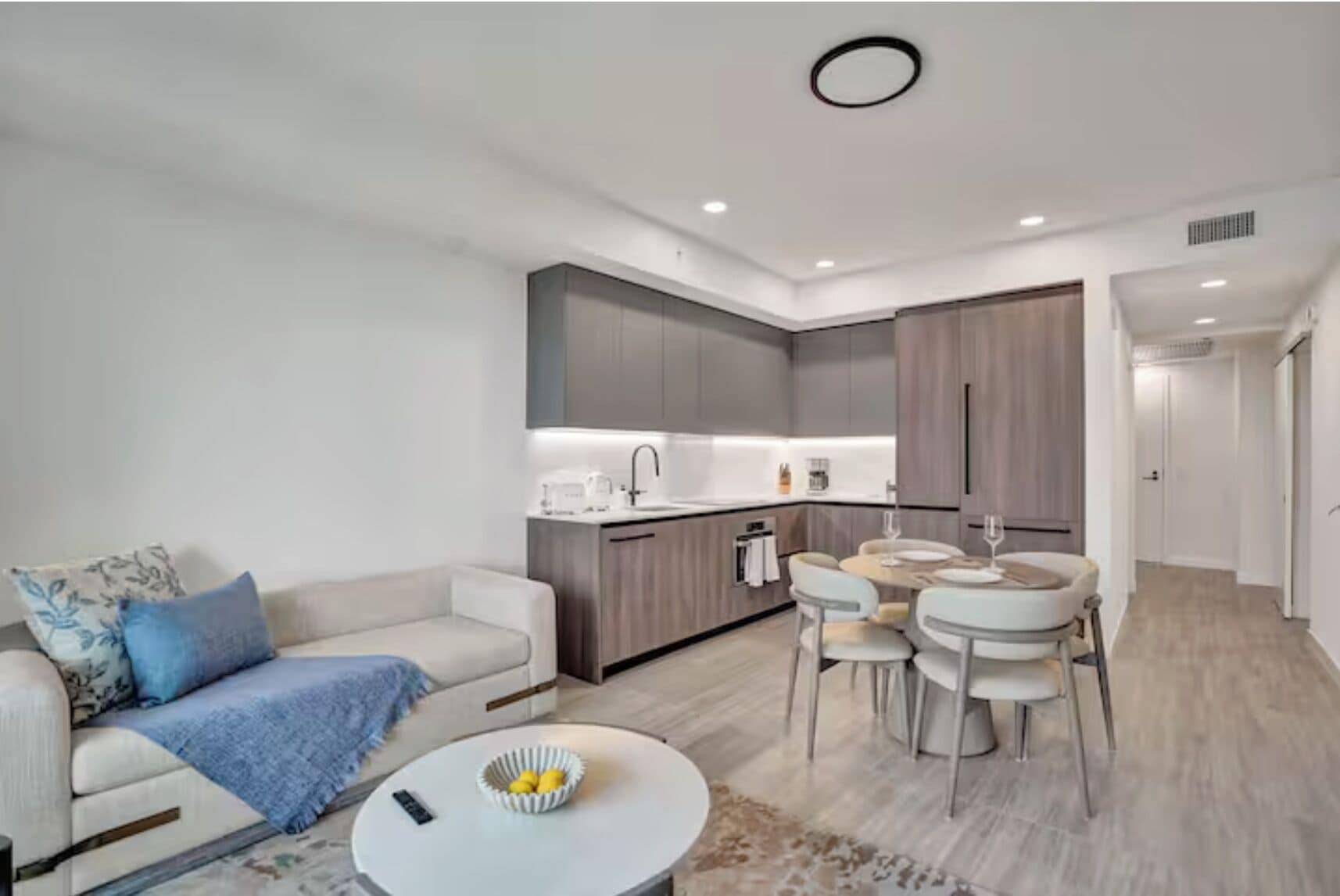 A modern living room with a sofa, coffee table, and a dining area with chairs and a table.