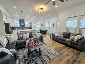 A modern living room with a sofa, coffee table, and a dining area in the background. - Blue Turtle Inn - Sleeps 16, EV Charger, near the beach! (Bolivar Peninsula)